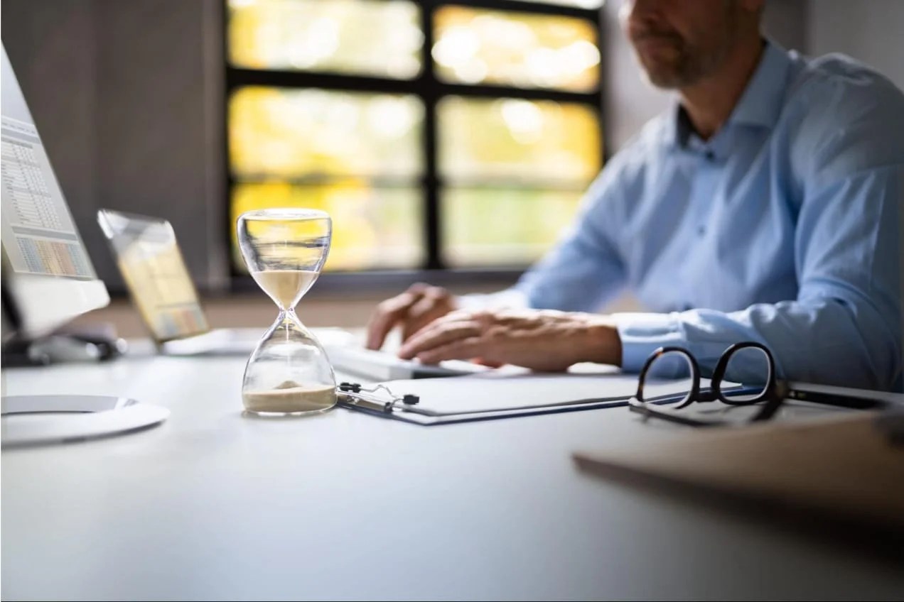 A man works on a spreadsheet in his office, halfway through the hourglass.